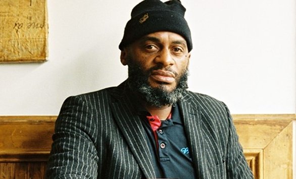 Michael Thompson, owner of Brooklyn Moon, sitting at a table and looking at the camera wearing a striped blazer and a black knit hat.