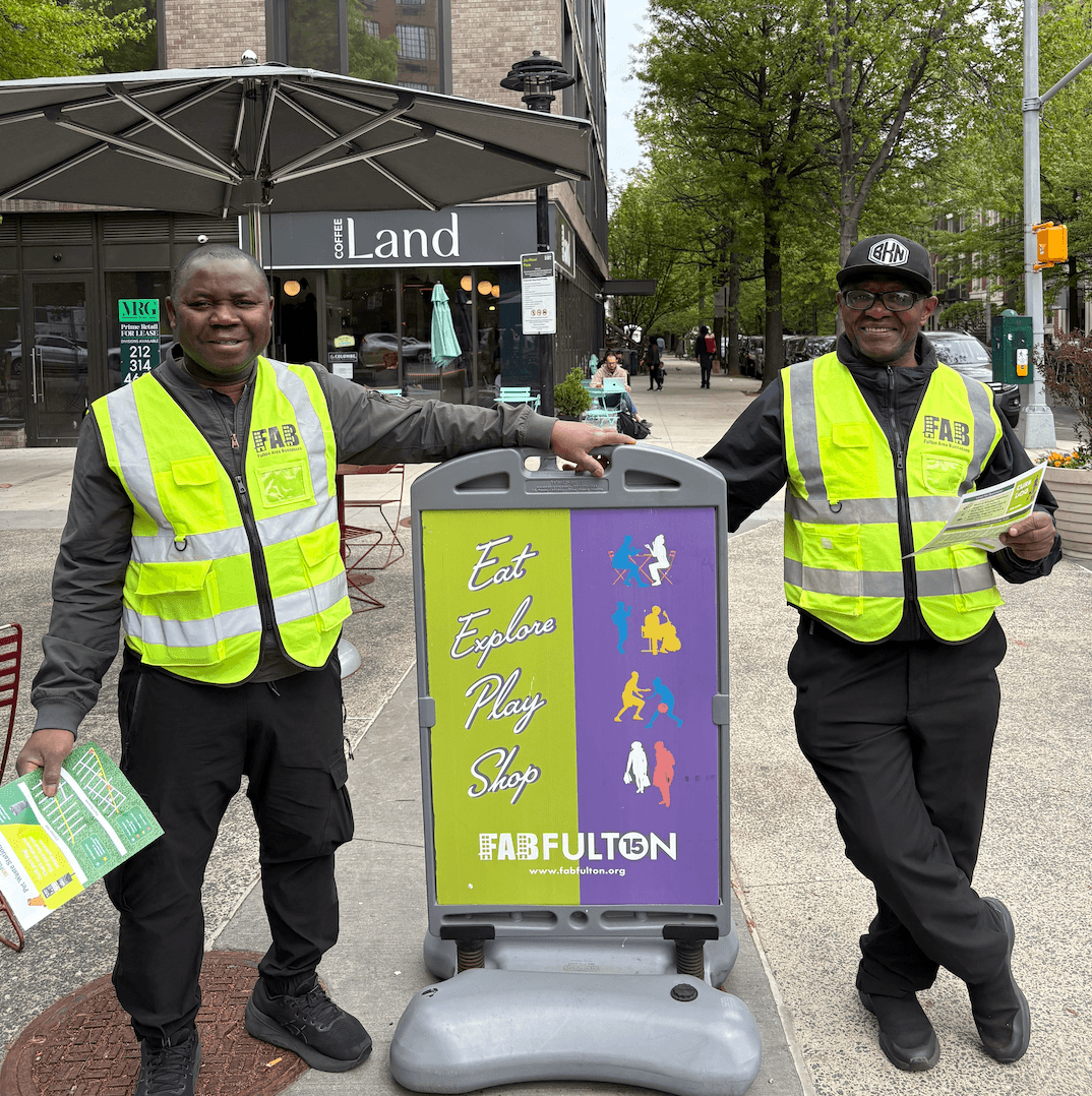 Two uniformed safety ambassadors standing in Jitu Weusi Plaza near the FAB sign