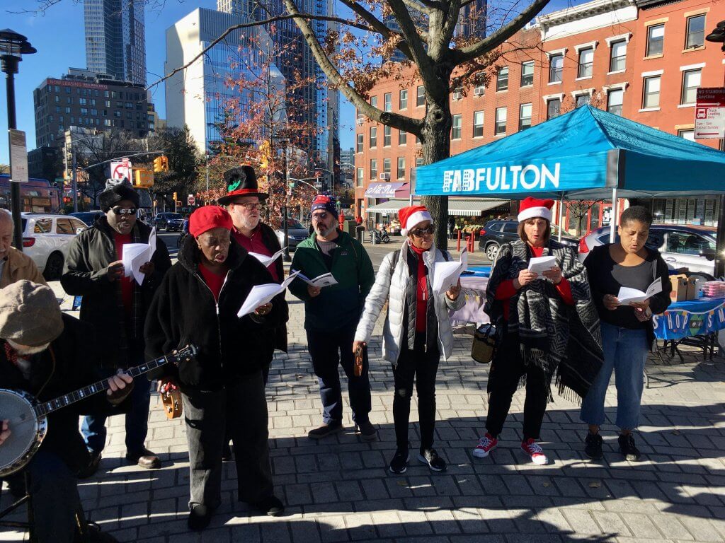 Scene from past holiday caroling event with singers in the plaza
